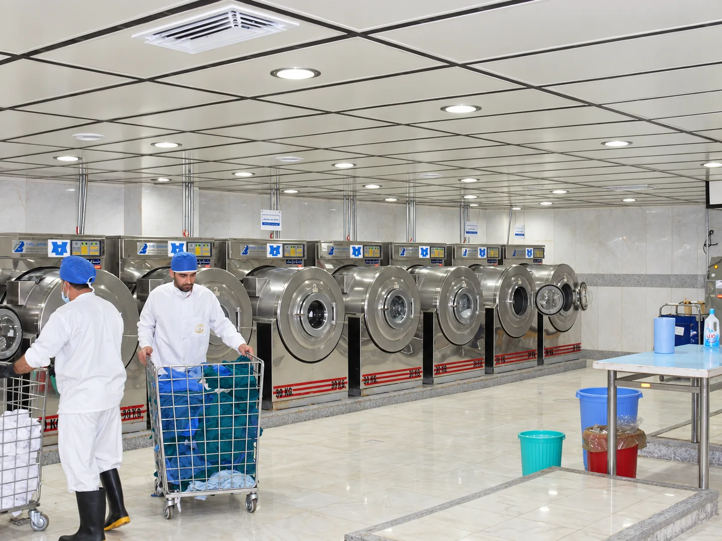 Main washing area of the Baqiyatallah Hospital laundry with industrial machines and linen carts