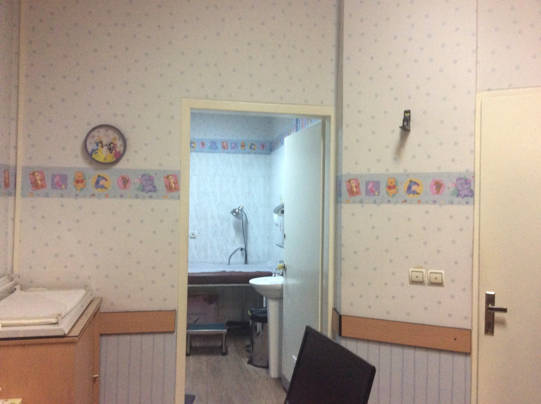 Day Hospital pediatric clinic room before renovation with older clinical finishes, doorway and examination equipment