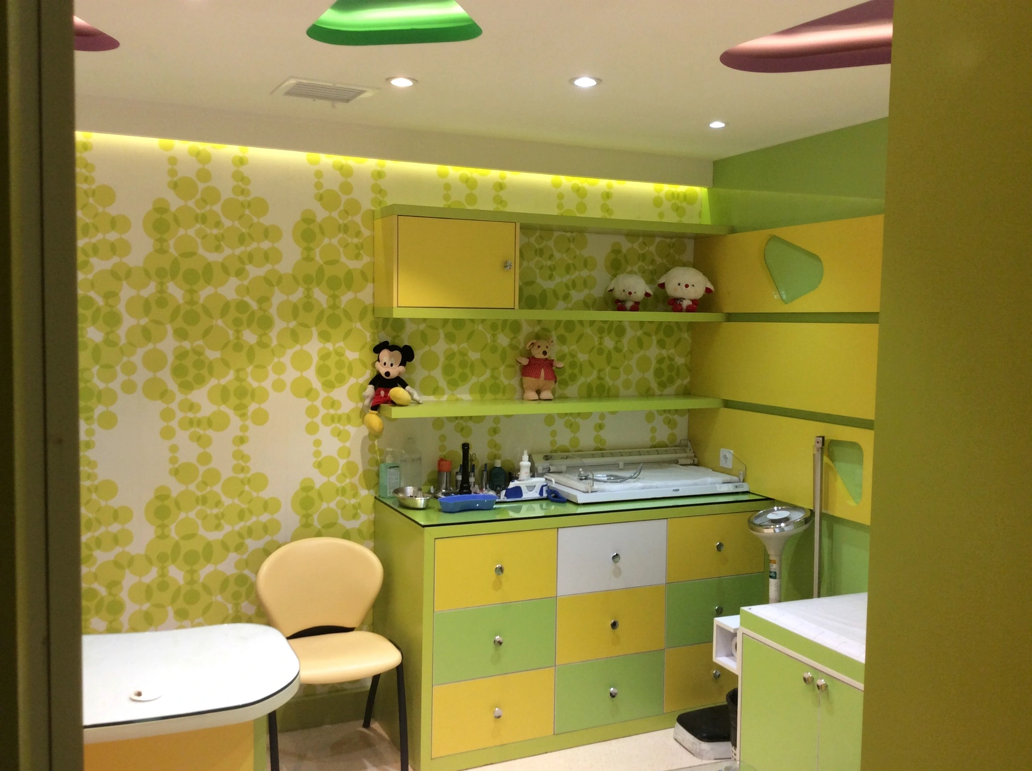 Pediatric examination counter at Day Hospital with built-in shelves, green-yellow cabinetry and child-themed interior details